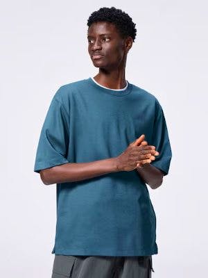 A model wearing a teal crew-neck T-shirt with mid-length (5‑minute) sleeves.