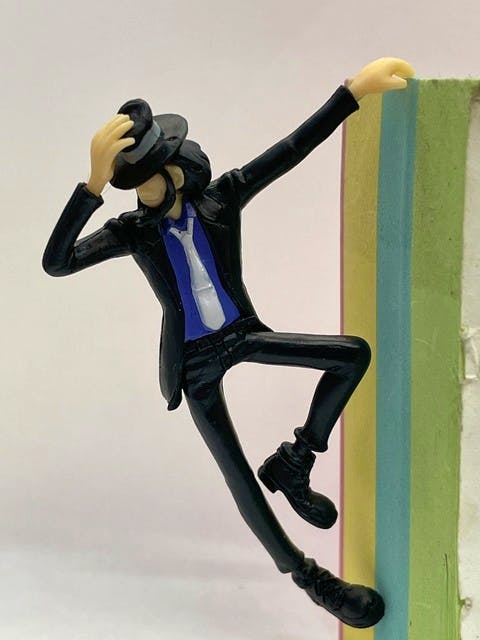 Plastic figure of Jigen Daisuke from Lupin III wearing a black suit and hat, posed leaning on a stack of colored pads.