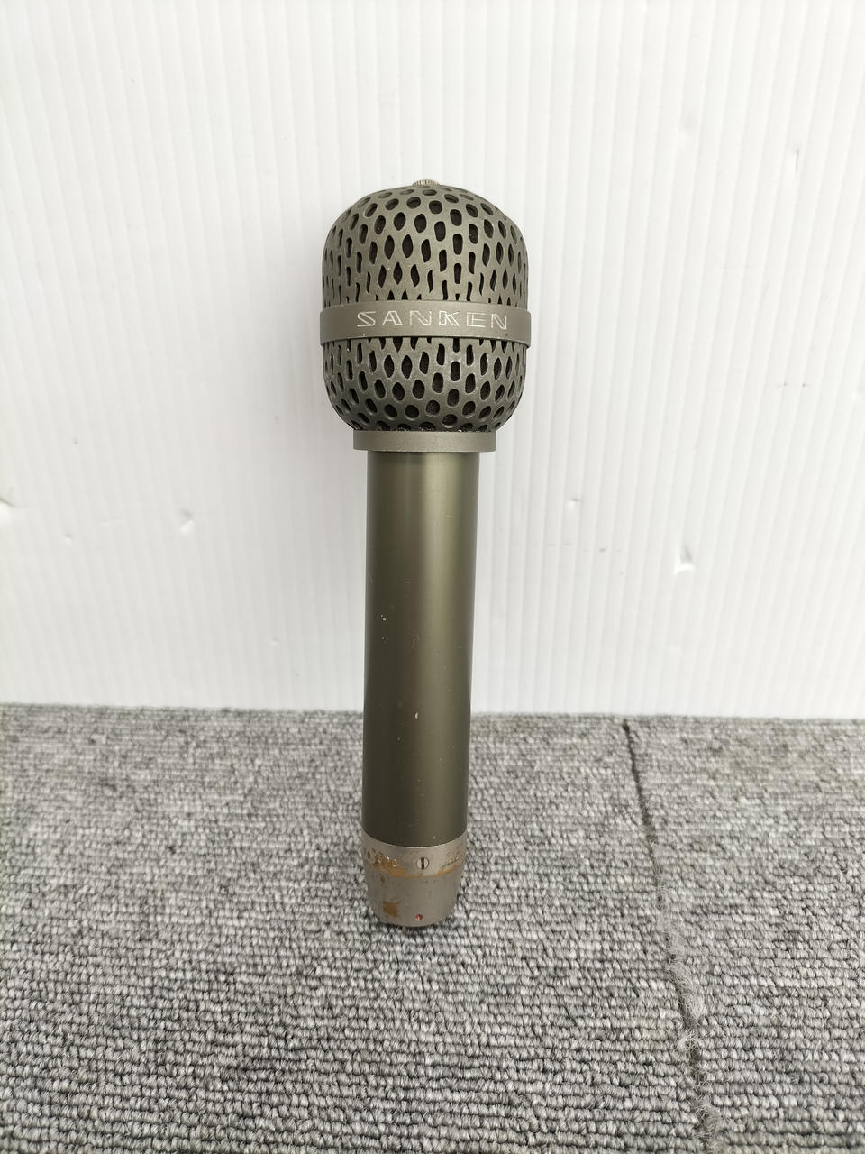 Handheld dynamic microphone standing upright on a carpeted surface against a white background.