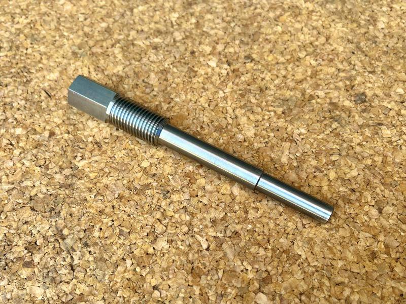 A metal dynamo rotor puller with a threaded shaft and hexagonal head placed on a cork surface.