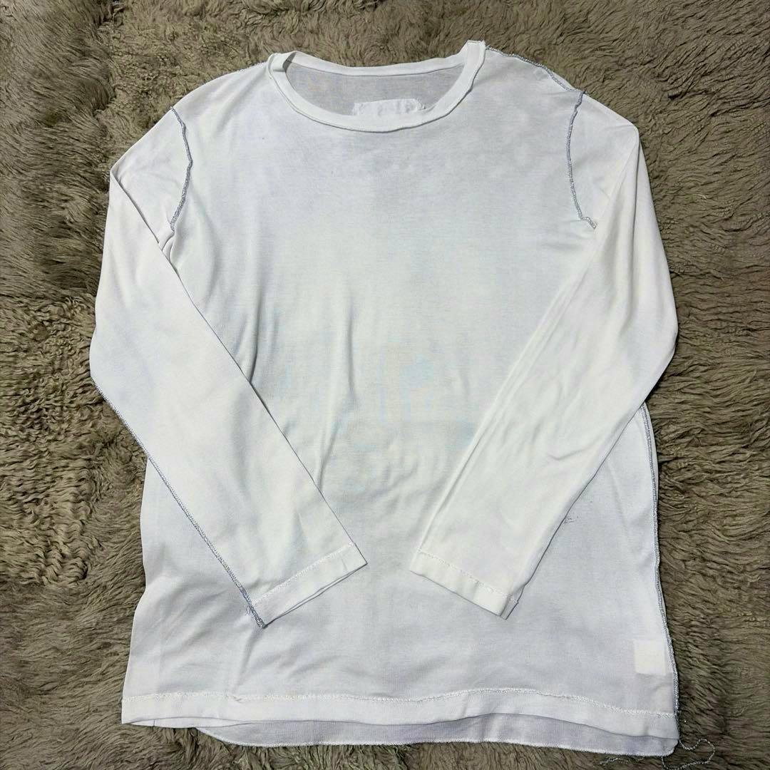 White long-sleeve cotton T-shirt laid flat on a textured surface showing visible inside-out seams.