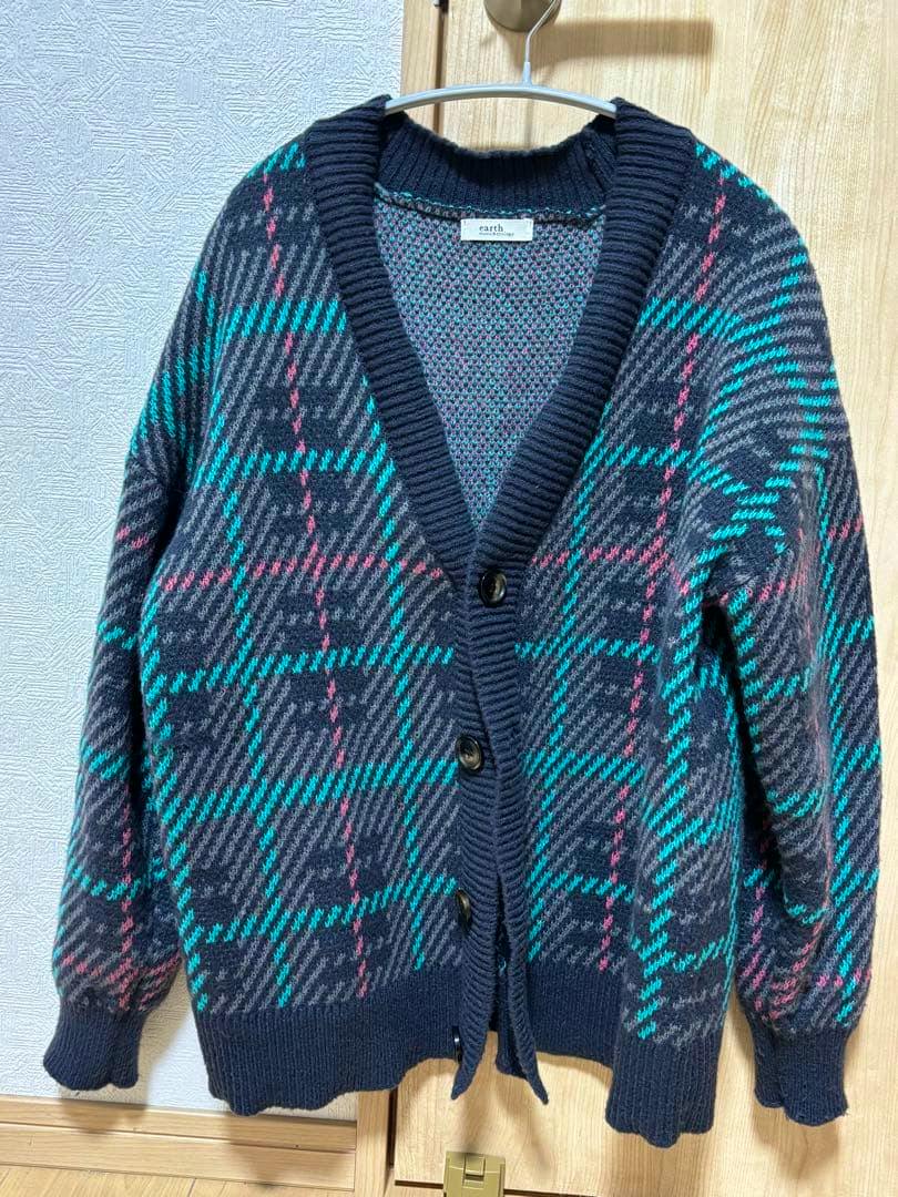 A check-pattern cardigan hanging on a hanger showing the front with buttons and long sleeves.