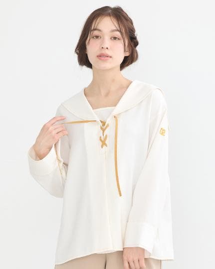 Model wearing a white sailor-style women’s blouse with gold lace-up detail at the neckline.