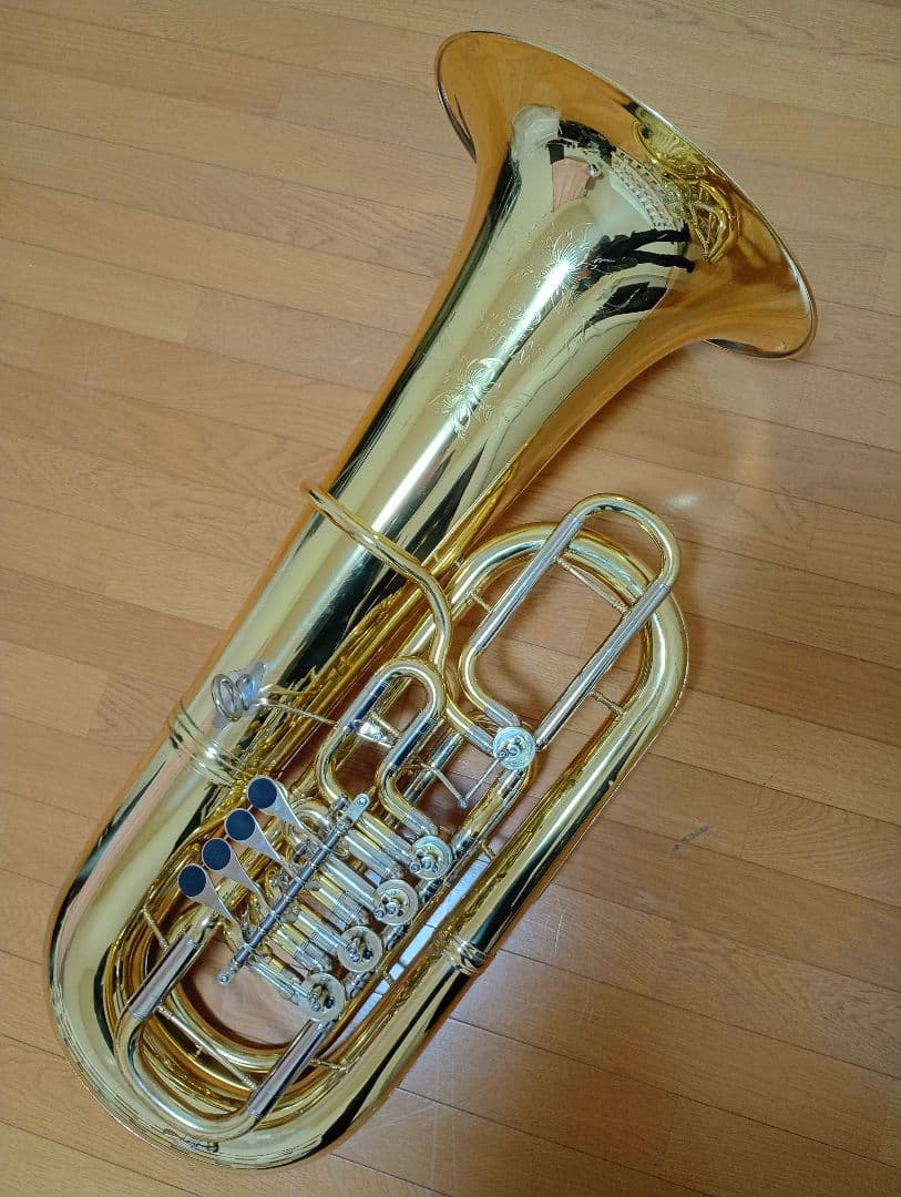 A brass EASTMAN EBF‑864 F tuba lying on a wooden floor showing the bell and valve section.