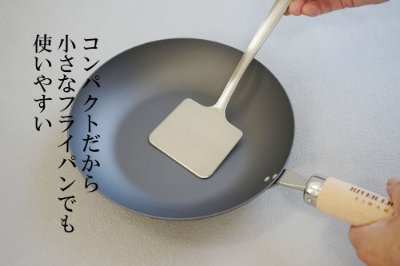 A metal turner positioned in a small frying pan being held by a hand.