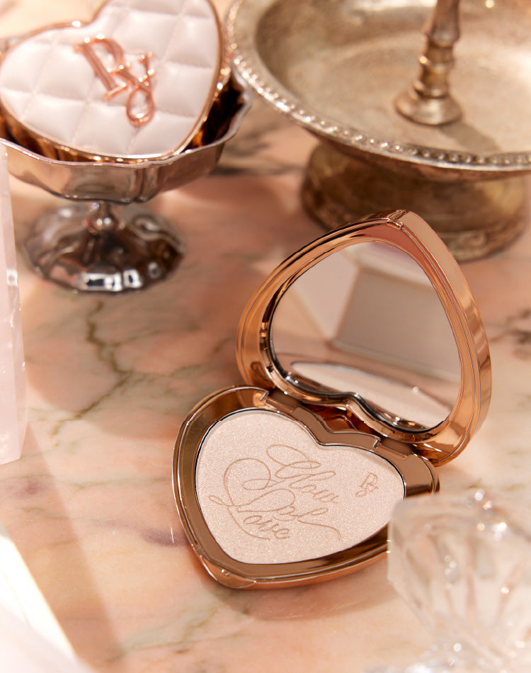 Open heart-shaped compact of the foundation '02 Eclat Amour' showing embossed powder and a mirror on a marble surface.