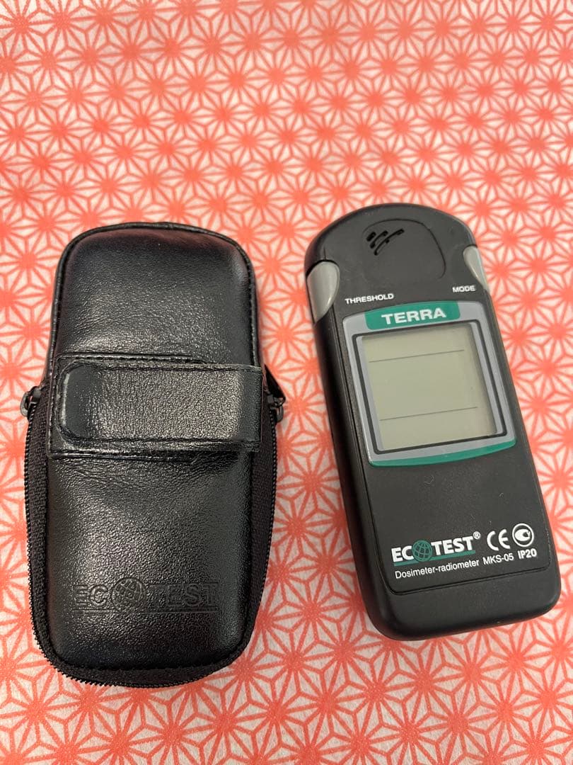 ECOTEST MKS-05 radiation detector (TERRA) shown next to its black carrying case on a red-and-white patterned surface.