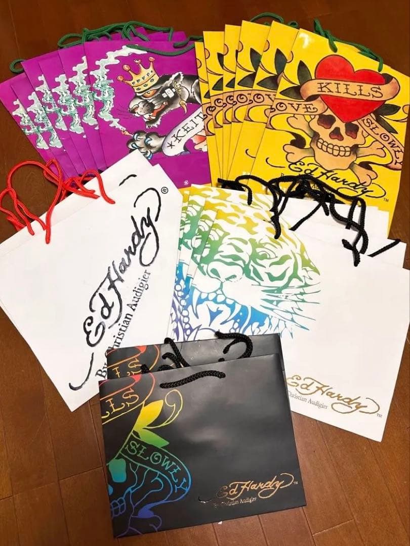 Several Ed Hardy paper shopping bags in different designs and colors arranged on a wooden floor.