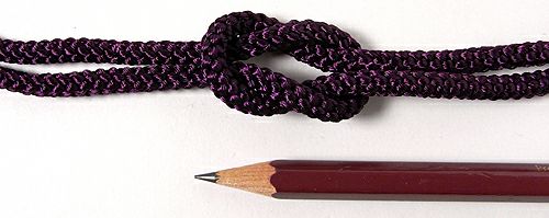 Close-up of a deep purple braided cord (5mm) tied in a knot shown above a pencil for scale.