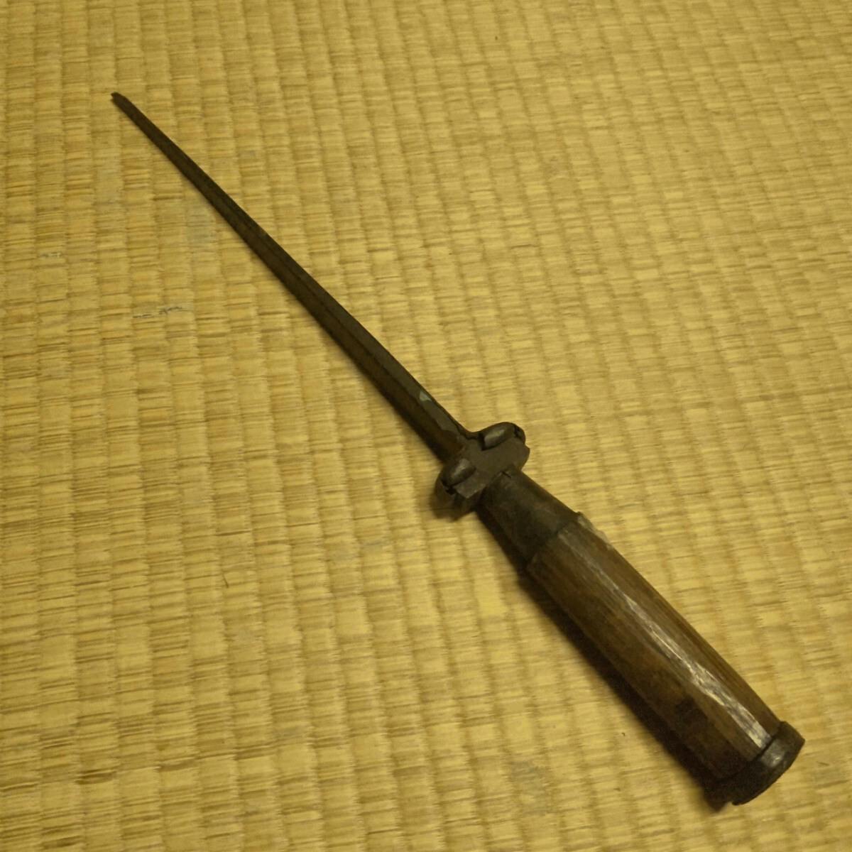 A metal carving knife with a long narrow blade and wooden handle lying on a tatami mat.