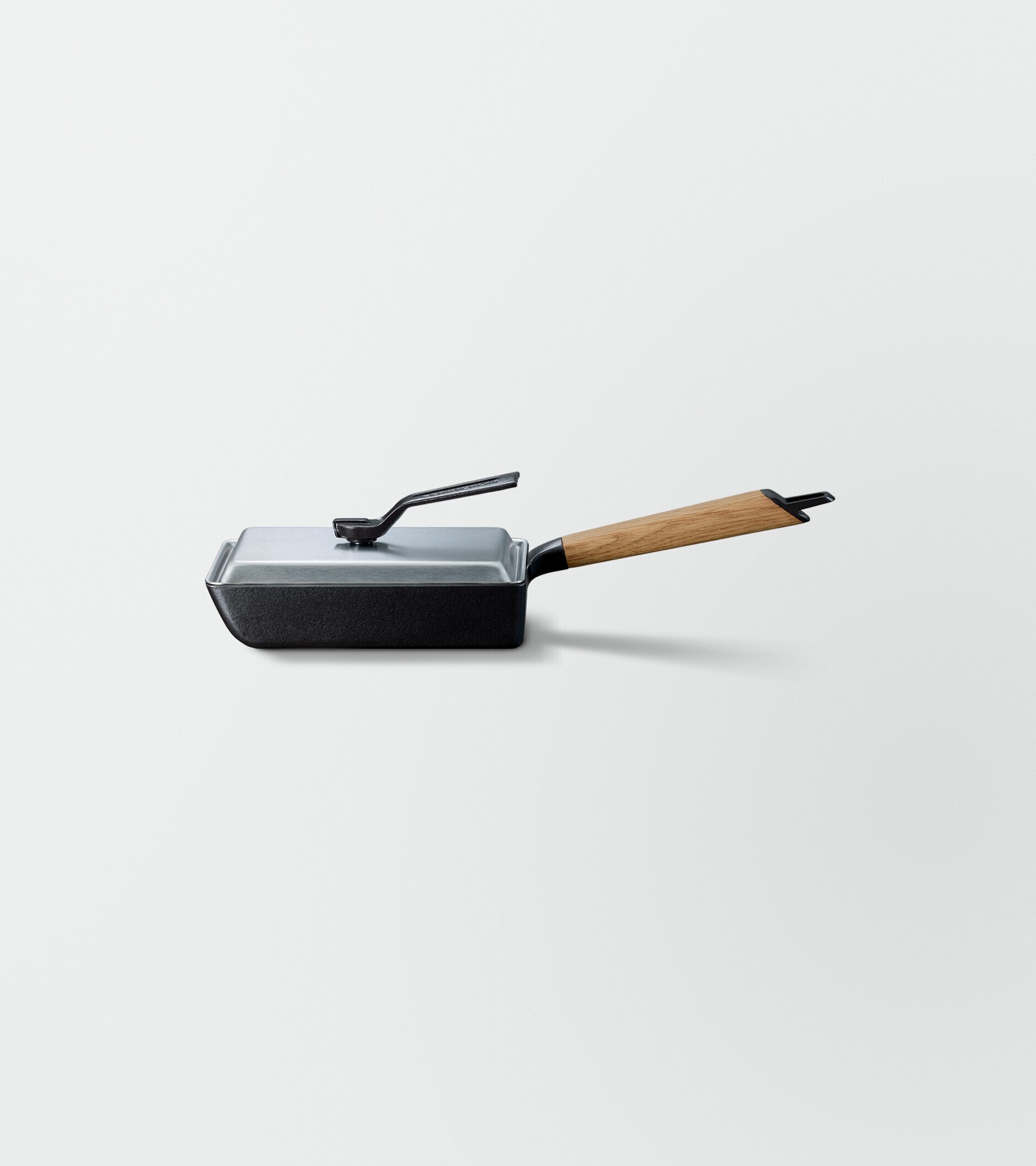 Side view of a rectangular frypan with a wooden handle and a stainless lid on top.