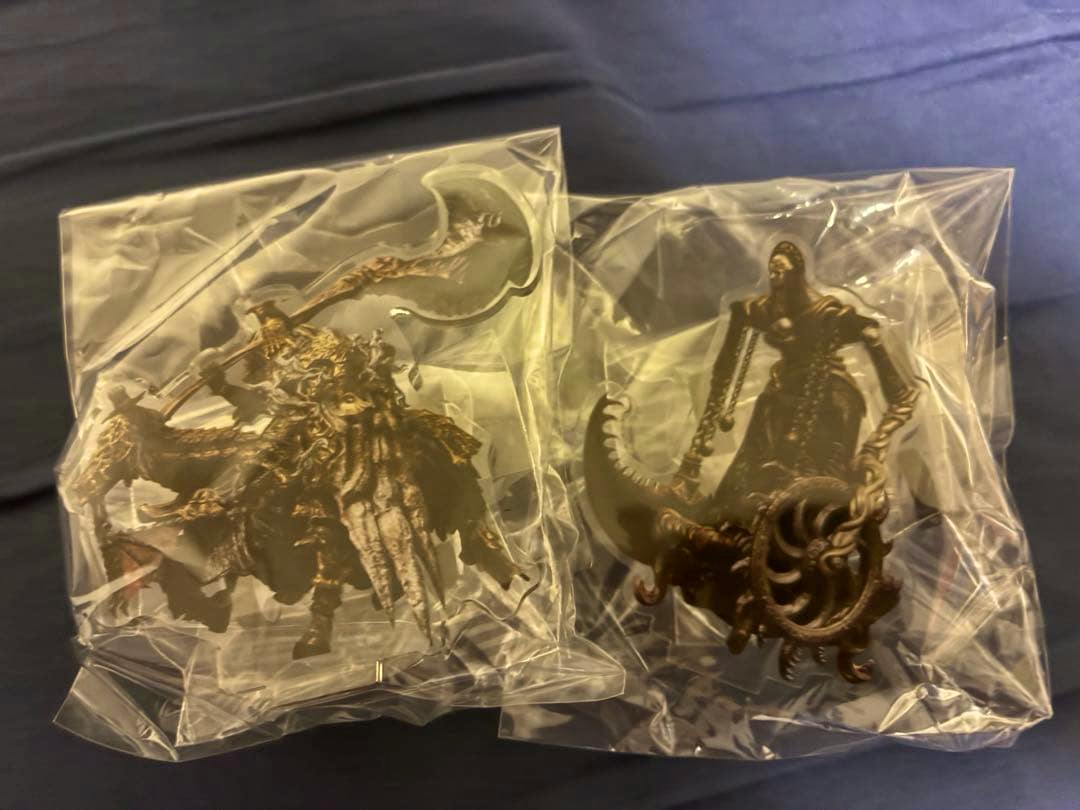 Two Elden Ring acrylic decorative stand figures sealed in clear plastic bags on a dark surface.