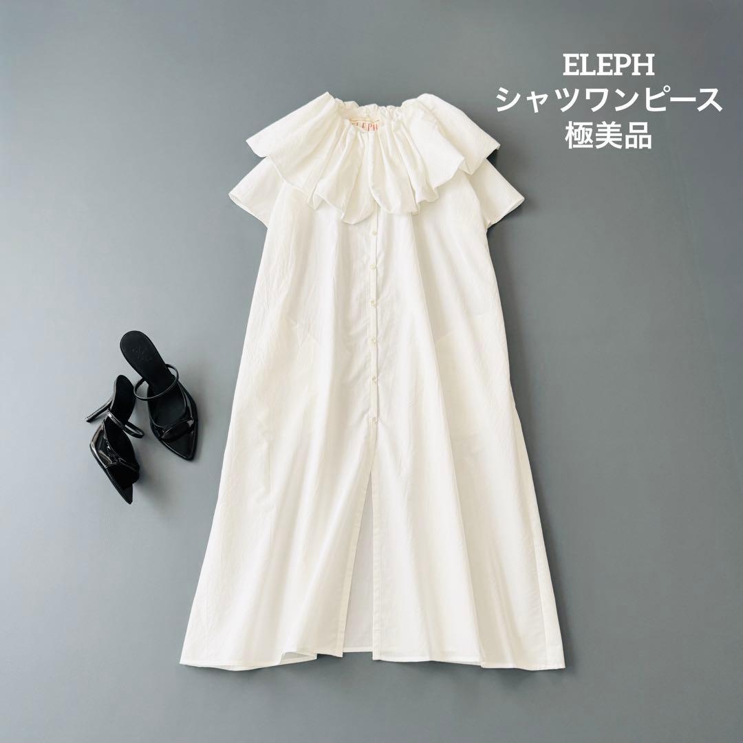 White ELEPH short-sleeve dress with a large ruffled collar laid flat next to black heels.