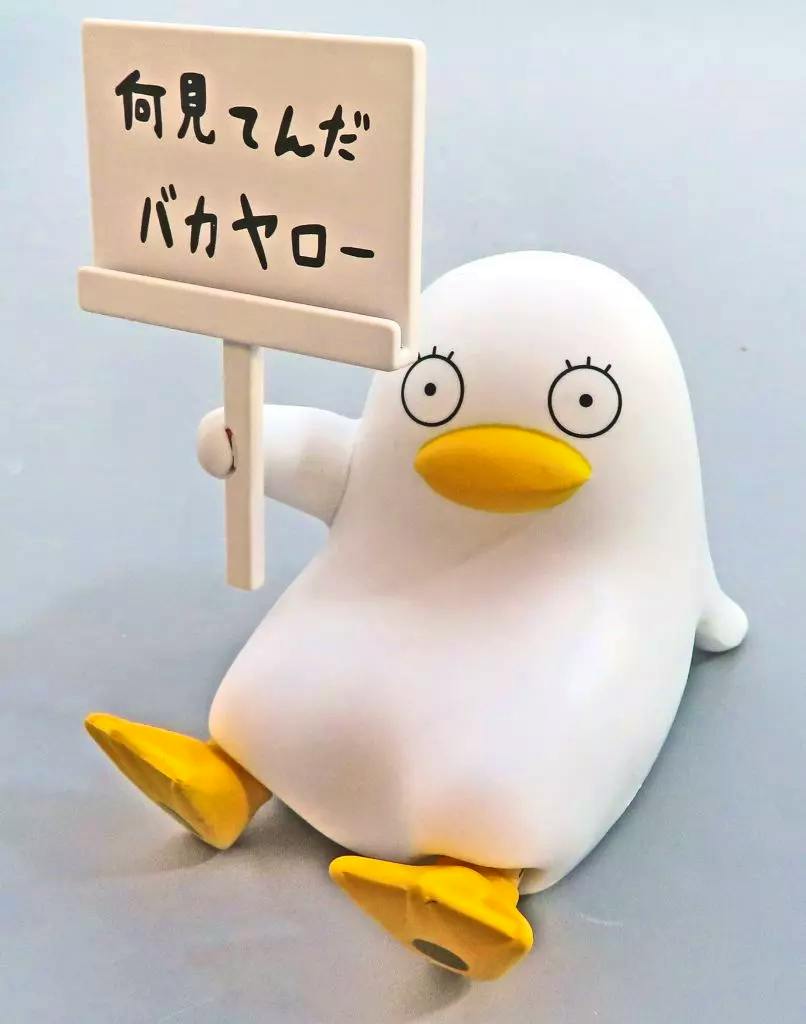 White Elizabeth mascot plastic figure from Gintama, sitting and holding a small sign with Japanese text on a gray surface.