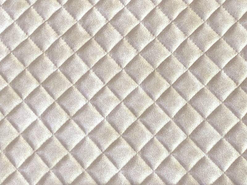 Close-up of beige glossy quilted diamond-pattern embossed synthetic leather fabric (polyester).