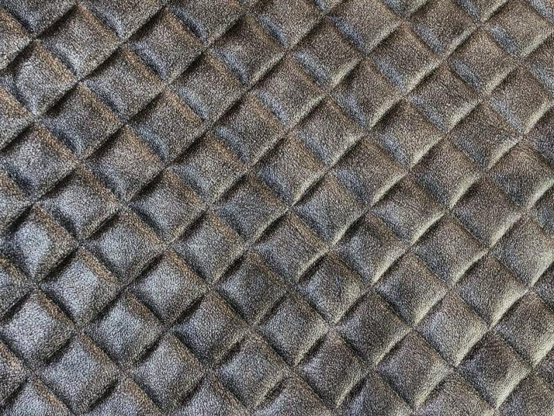 Close-up photo of charcoal embossed faux leather (polyester) fabric with a glossy quilted diamond pattern.