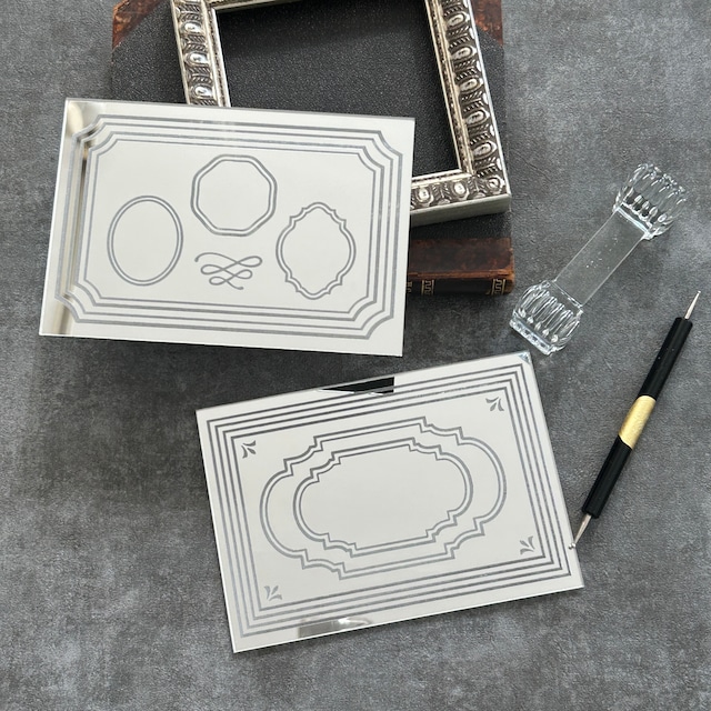 Metal embossing template plate with postcard-frame designs displayed alongside another template and embossing tools on a gray surface.