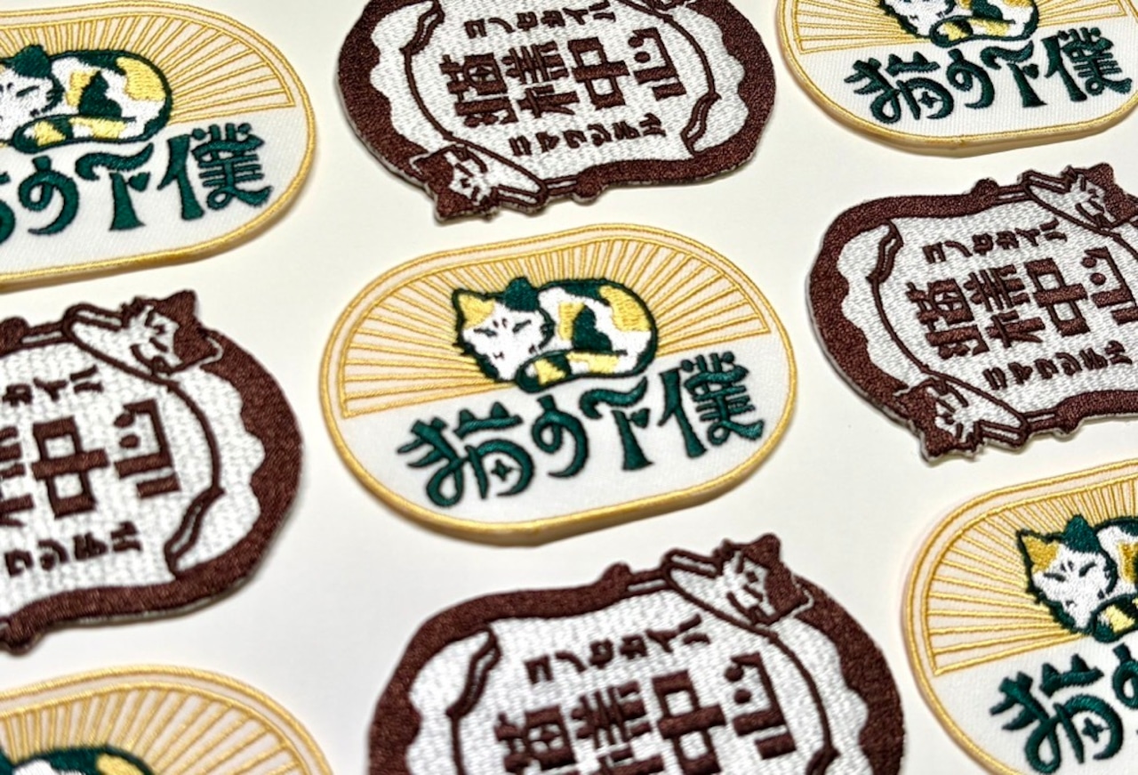 Multiple oval embroidered fabric patches showing a sleeping cat and Japanese text on a white background.
