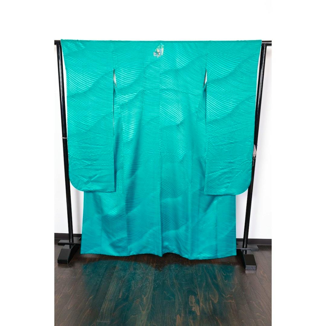 Emerald green women's furisode kimono with a subtle wavy woven pattern displayed hanging on a stand.