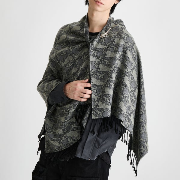 A model wearing the patterned wool scarf draped over the shoulders and secured with a decorative scarf pin.