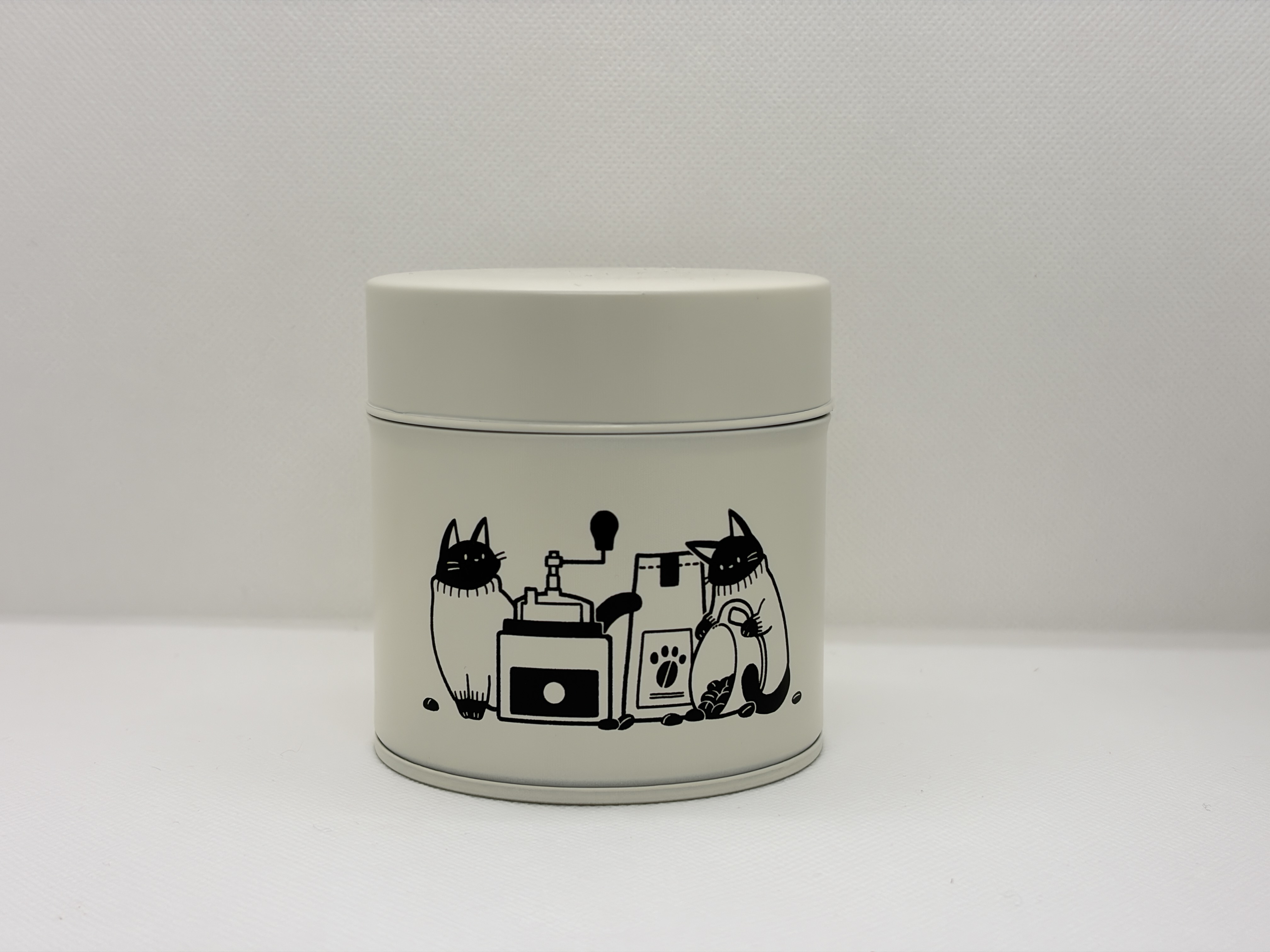 A cream-colored empty coffee can with a cat and coffee grinder illustration on a plain background.