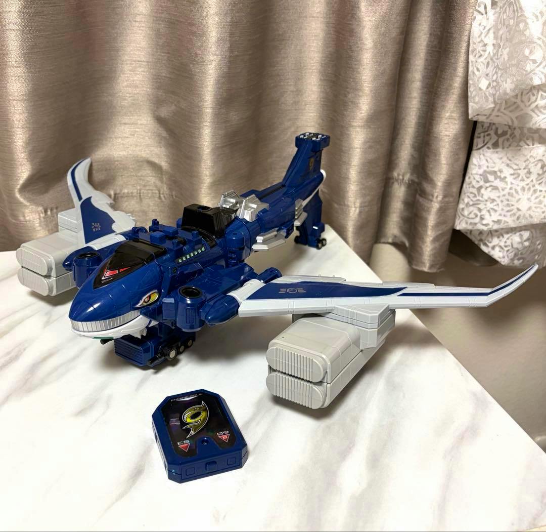 A blue-and-white plastic DXエンジンジャンボエール toy airplane is shown on a table with a small blue accessory placed in front.