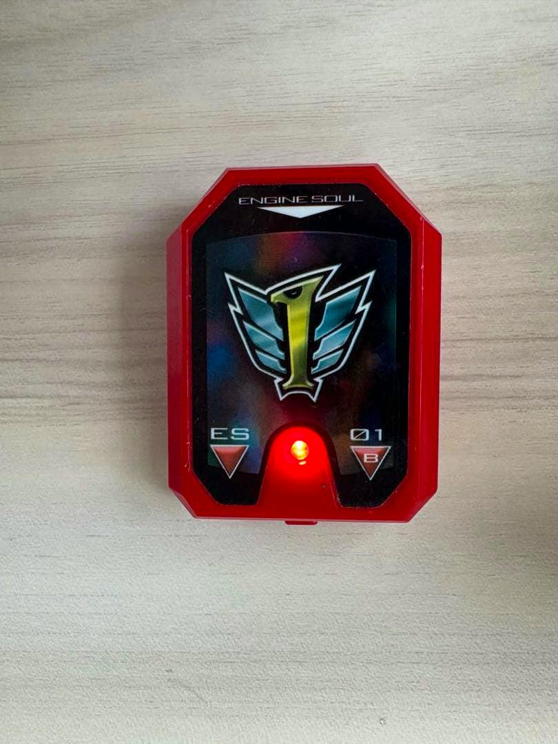 Red plastic 'Engine Soul 01' toy piece with a winged number one emblem and a lit red LED on a wooden background.