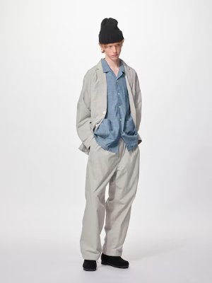Male model wearing light-colored easy pants and a jacket on a white background.