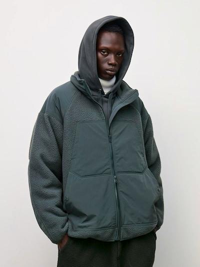 A model wearing the fleece hooded oversized vest from ENGINEERED GARMENTS, shown front-on with hands in pockets.