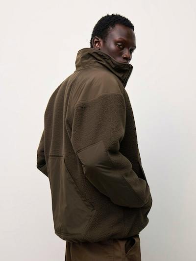 Rear three-quarter view of a model wearing an olive fleece utility jacket showing the back and high collar.