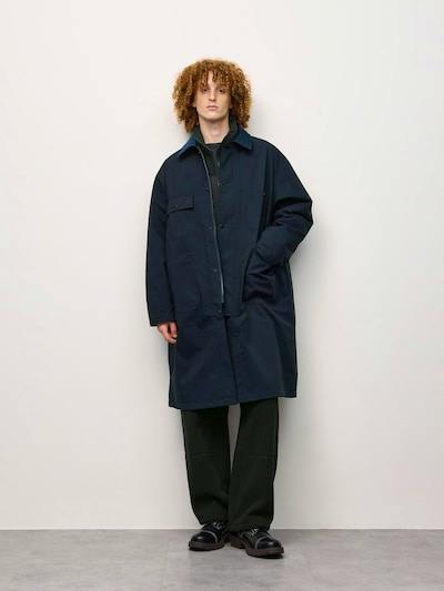 Model wearing an oversized padded work coat standing against a plain light background.
