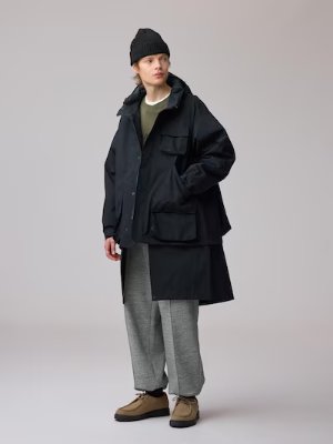 A model wearing the dark padded shell parka (men's jacket) styled with trousers and a beanie.