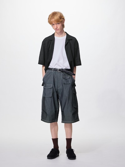 A male model wearing grey utility shorts with multiple cargo pockets, shown with a white t-shirt and a short black overshirt.