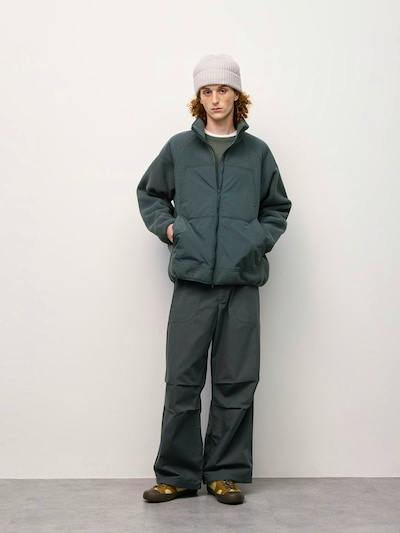 Male model standing against a plain background wearing the men's wide utility pants with a jacket and beanie.