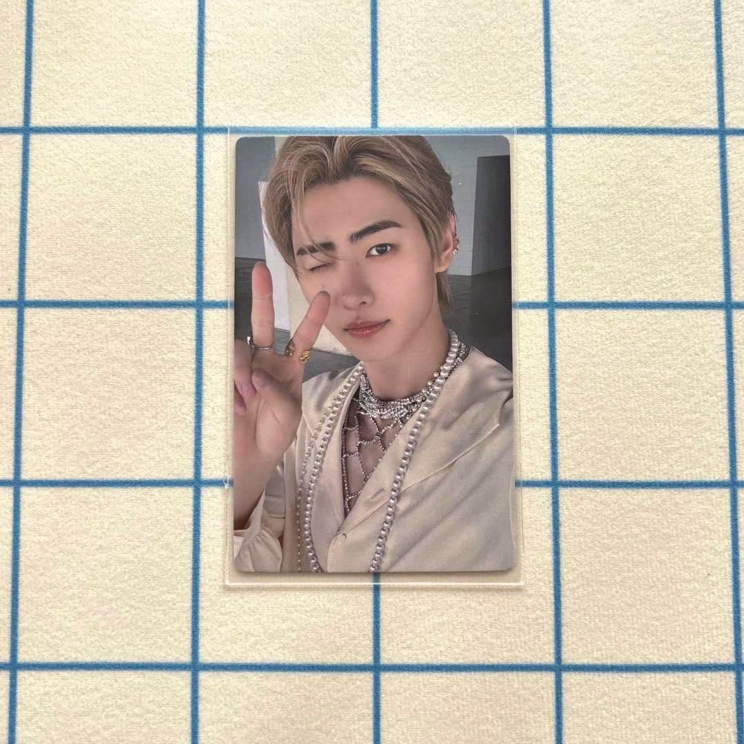 Front of a photocard showing a person winking and holding up a peace sign on a grid background.