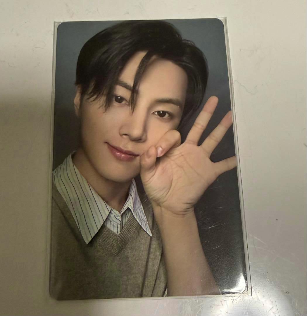 An ENHYPEN photocard in a clear plastic sleeve showing a close-up portrait of a young man with his hand raised beside his face.