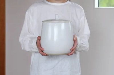 A person wearing a white top holds a white ceramic 4‑liter kame (pot) with both hands in front of their torso.