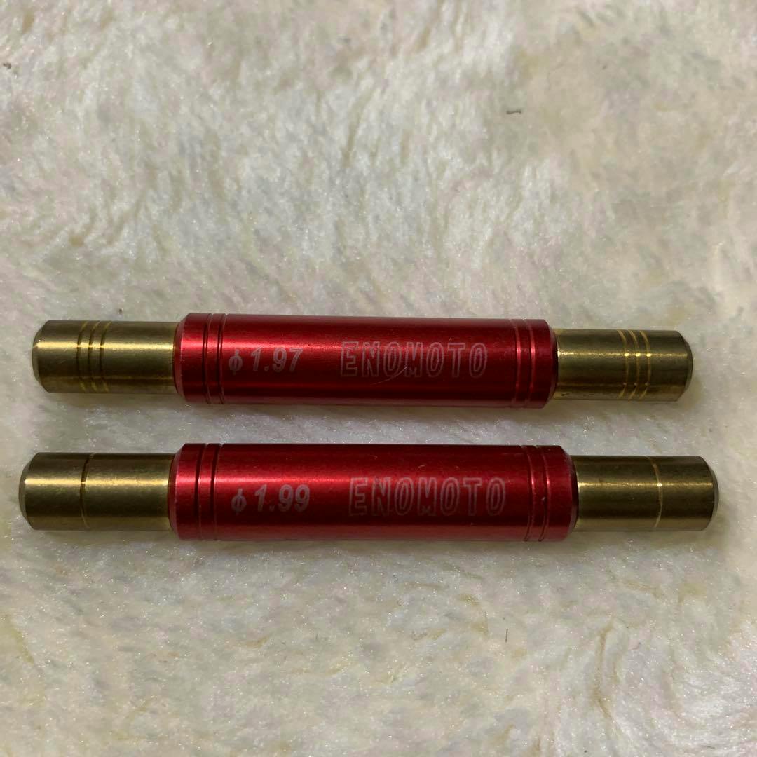 Two red ENOMOTO shaft checker tools with brass end caps placed on a light textured surface.