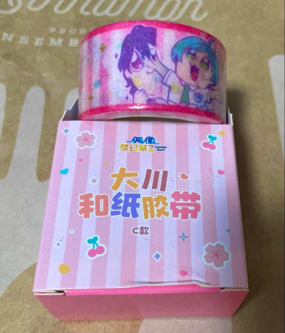 A roll of pink masking tape printed with chibi anime character illustrations placed on top of a pink striped box.