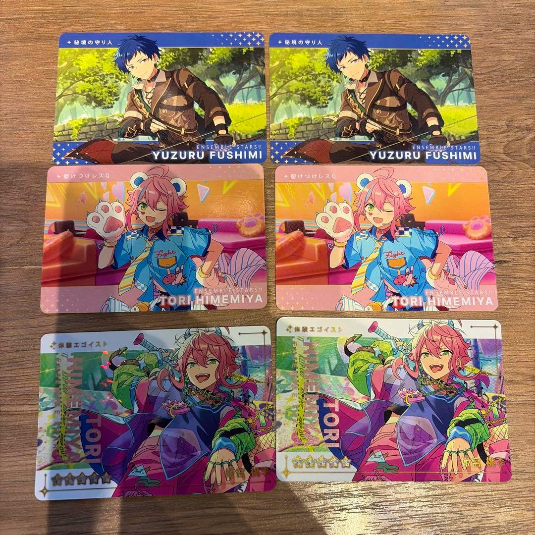 Six photocard trading cards of Ensemble Stars! characters including Yuzuru Fushimi and Tori Himemiya arranged on a wooden surface.