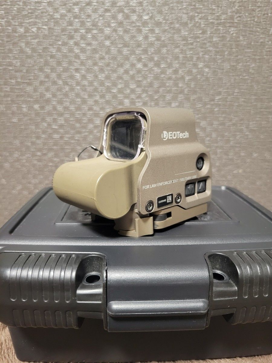 Tan EOTech EXPS3-0 holographic sight placed on a closed hard carrying case, front-left view showing buttons and lens.
