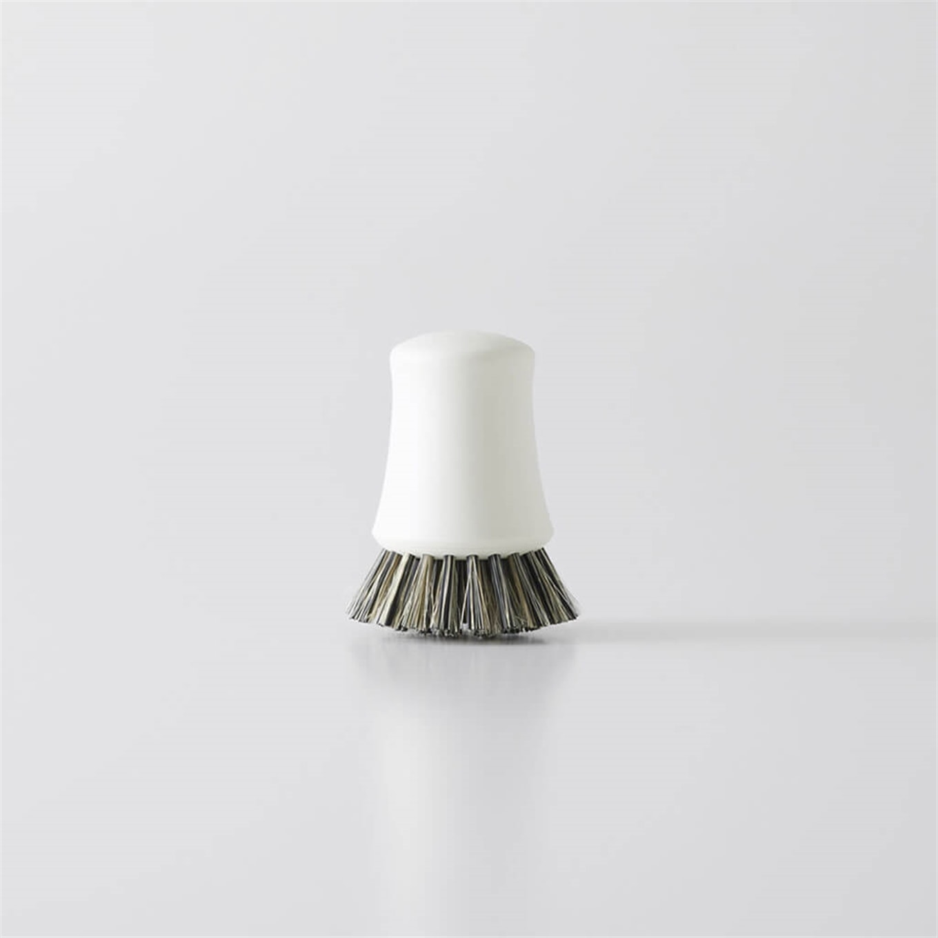 Small white handheld kitchen cleaning brush with short dark bristles on a plain light background.