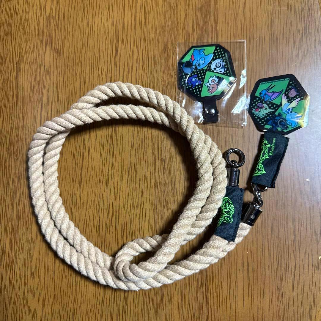 Beige twisted rope smartphone shoulder strap with metal clips and two decorative hexagonal charms on a wooden surface.