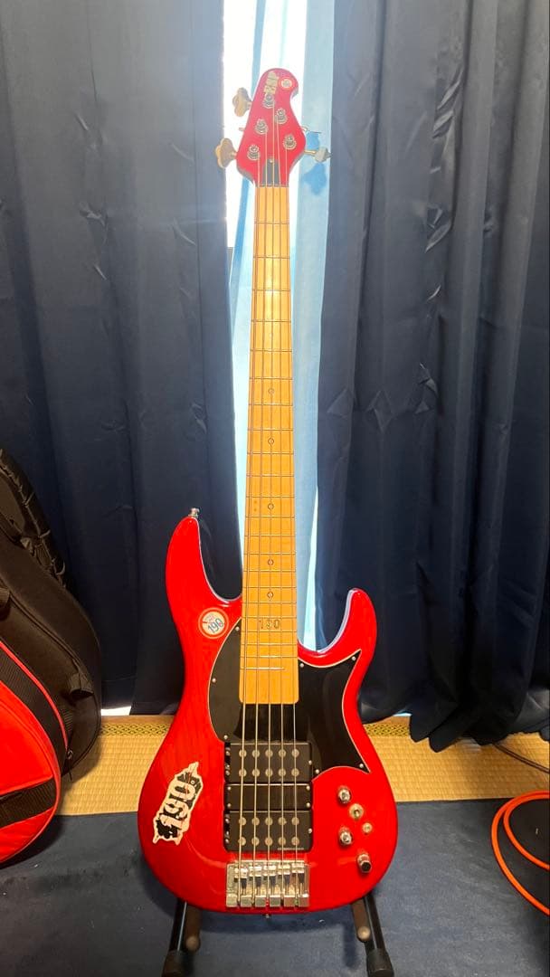 Front view of an ESP IKUO LONGWAY bass guitar in red on a stand against dark curtains.