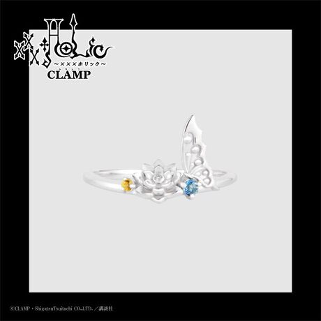 Silver ring with a small flower and butterfly-wing motif and two tiny yellow and blue stones on a white background with an xxxHOLiC logo.