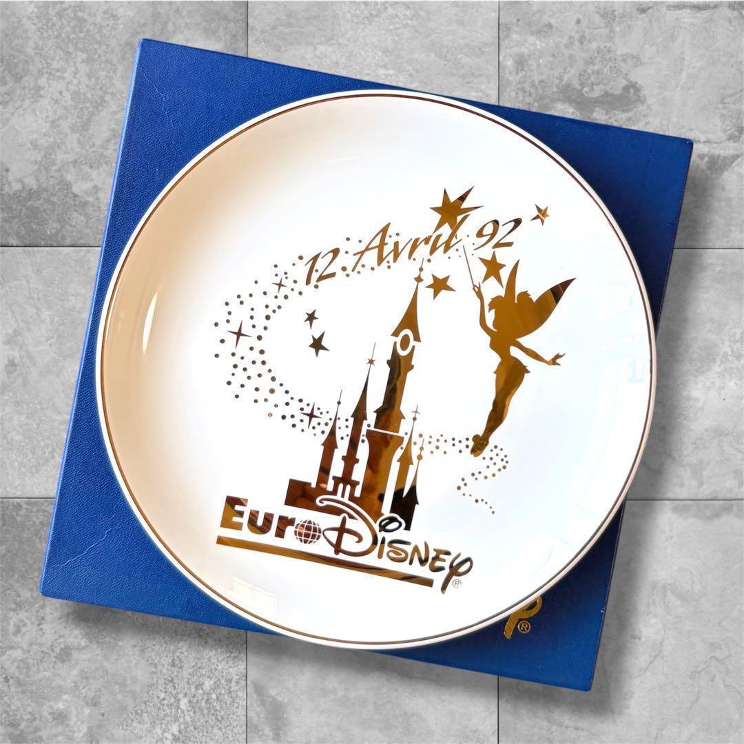 White Euro Disney 1992 commemorative ceramic plate with gold-tone Tinker Bell and castle design resting on a blue box.