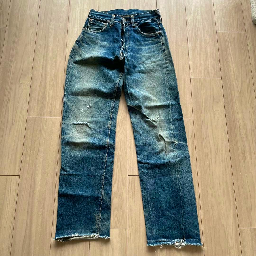 Front view of EVISU selvedge denim men's jeans (W28 approx) laid flat on a wood floor, showing a button fly, knee distressing, and frayed hems.
