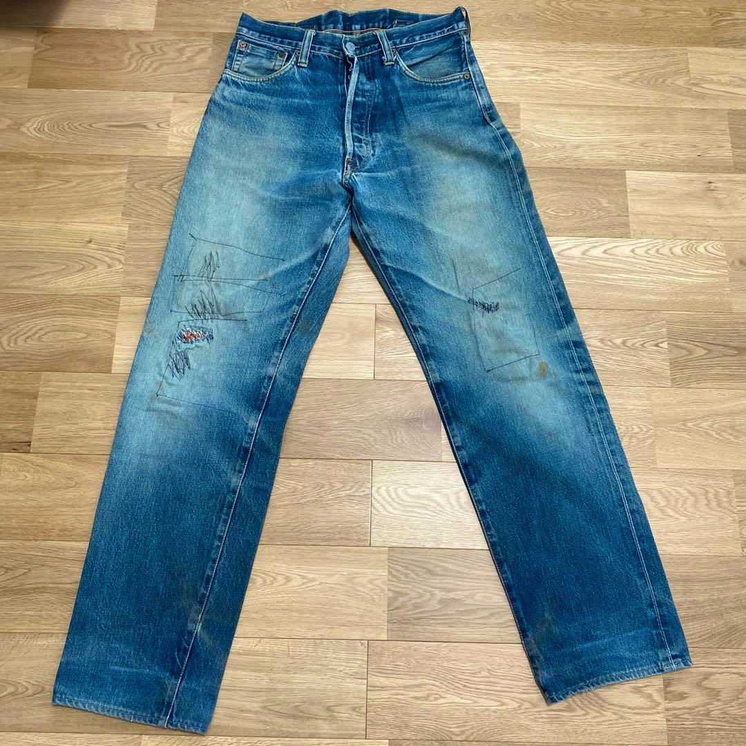 Front view of EVISU men's blue denim jeans (W32) laid flat on a wooden floor showing fading and visible repaired holes.