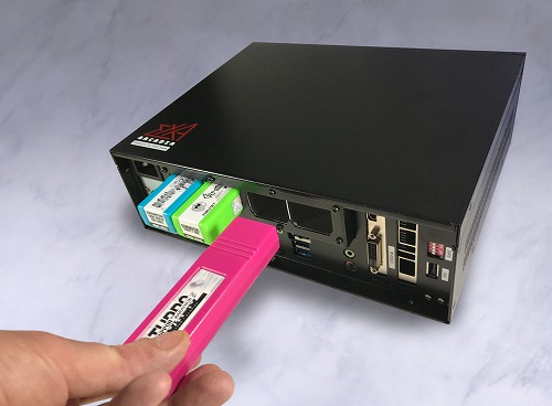 Rear view of the black exA-Arcadia EXA motherboard unit showing ports and a hand inserting a pink cartridge.