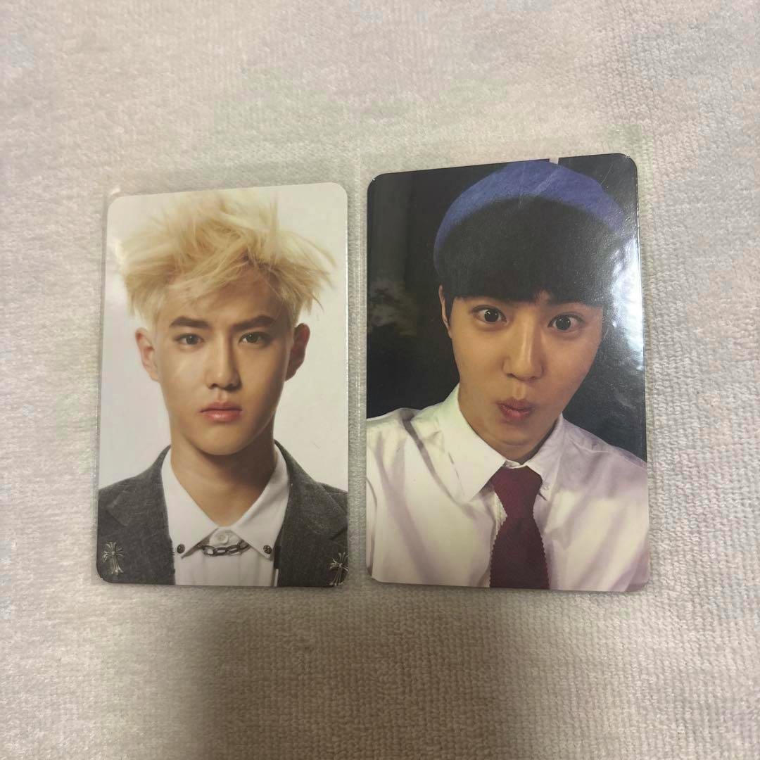 Two K-pop photocard cards showing frontal portrait photos of a male idol, placed side by side on a light fabric background.